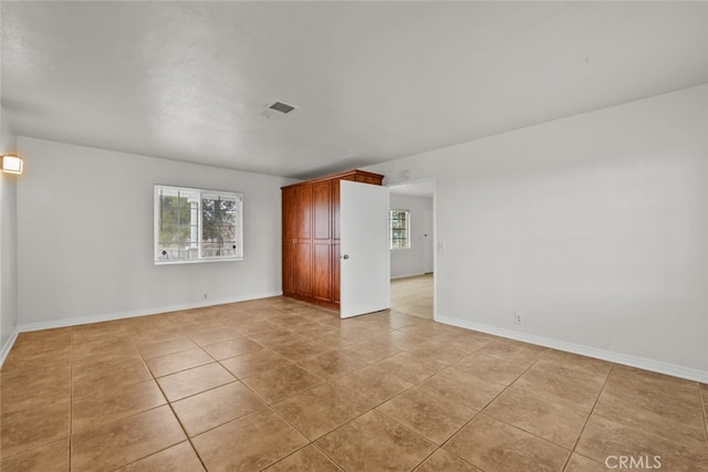 empty room featuring light tile patterned flooring, visible vents, and baseboards