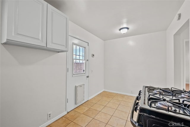 kitchen with light tile patterned floors, baseboards, white cabinets, and range with gas cooktop