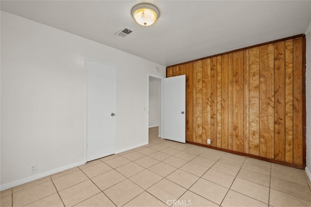 spare room featuring visible vents, wooden walls, baseboards, and light tile patterned flooring