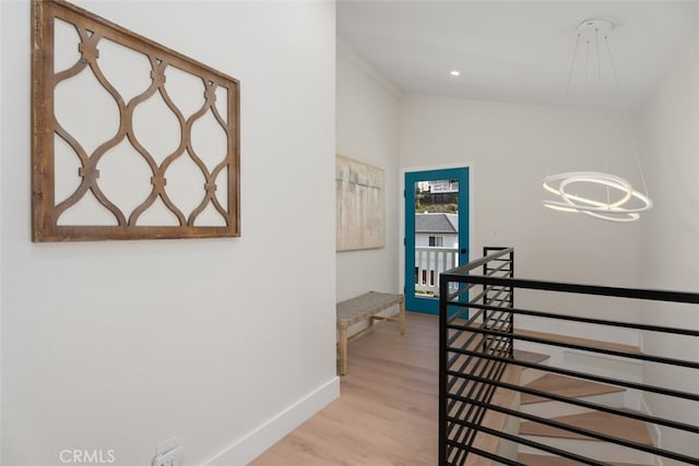 hallway featuring light wood-type flooring, baseboards, a chandelier, and lofted ceiling