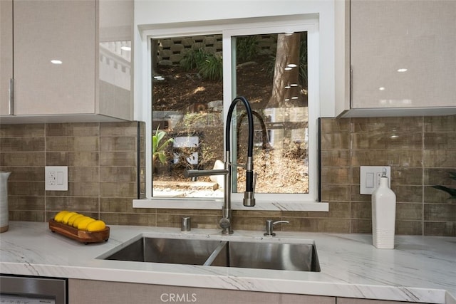 kitchen with dishwashing machine, tasteful backsplash, light stone counters, and a sink