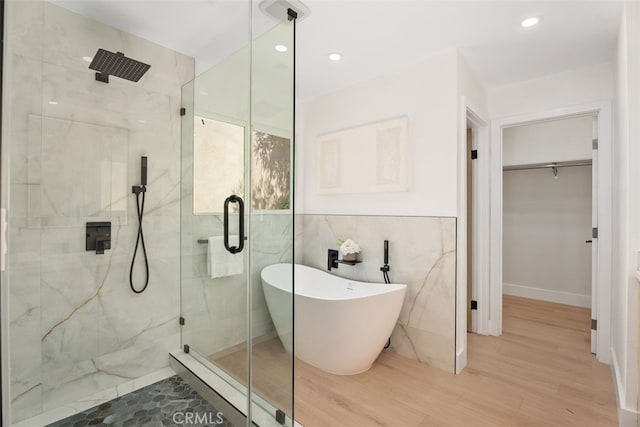 bathroom with tile walls, a freestanding tub, a spacious closet, and a marble finish shower