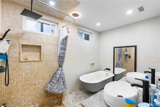 full bathroom with tile walls, visible vents, a freestanding bath, a sink, and tiled shower