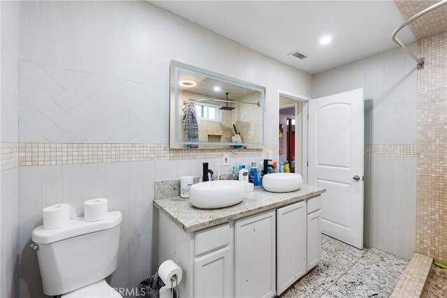 bathroom with toilet, visible vents, a tile shower, and tile walls