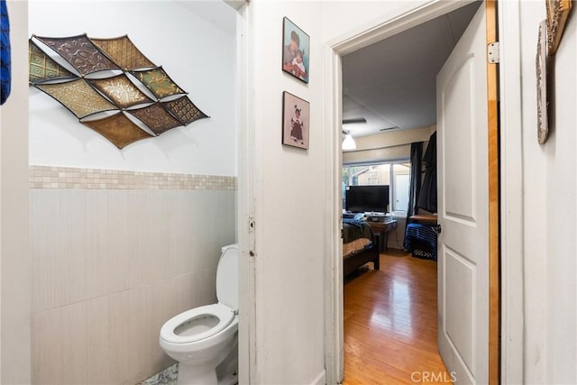 bathroom with wainscoting, tile walls, toilet, and wood finished floors