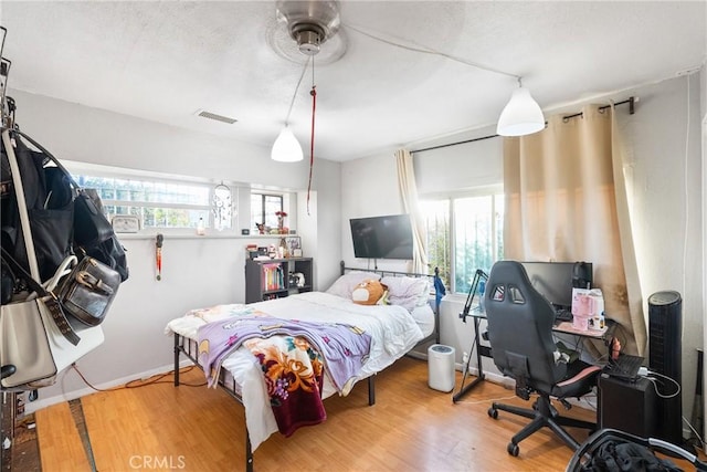 bedroom featuring baseboards, visible vents, multiple windows, and wood finished floors