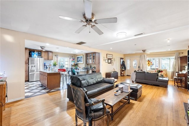 living room featuring baseboards, light wood finished floors, visible vents, and a healthy amount of sunlight