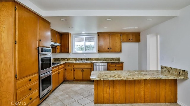 kitchen with brown cabinetry, appliances with stainless steel finishes, a peninsula, under cabinet range hood, and a sink