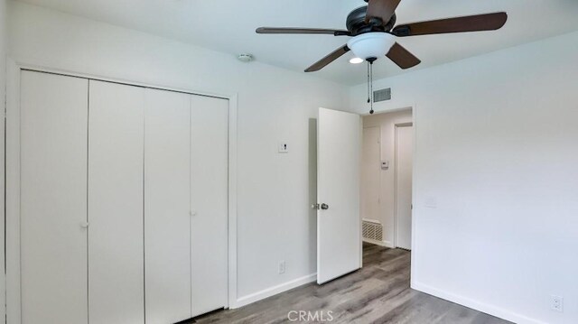 unfurnished bedroom with baseboards, a closet, visible vents, and wood finished floors