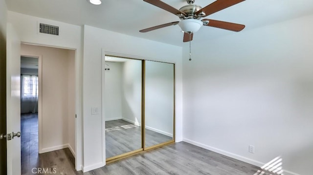 unfurnished bedroom with wood finished floors, a ceiling fan, visible vents, baseboards, and a closet