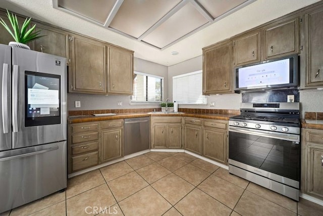 kitchen with dark countertops, light tile patterned floors, stainless steel appliances, and a sink