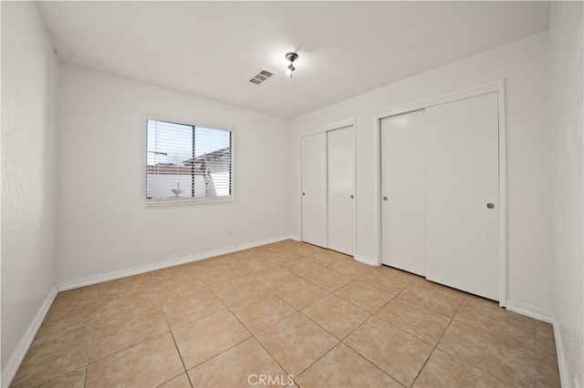 unfurnished bedroom featuring light tile patterned floors, baseboards, visible vents, and multiple closets