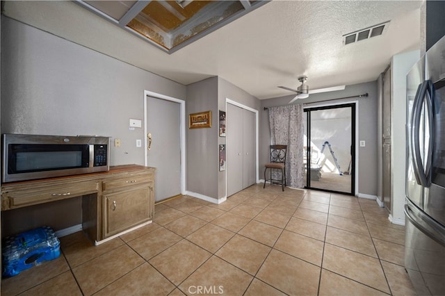 interior space with a textured ceiling, light tile patterned flooring, visible vents, a ceiling fan, and built in study area