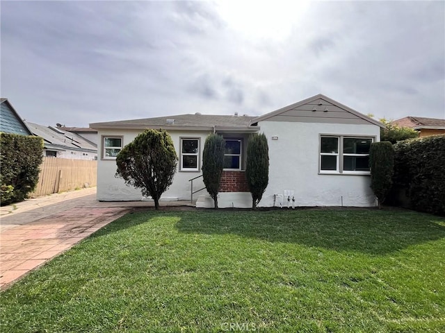 view of front of house featuring brick siding, fence, a front lawn, and stucco siding