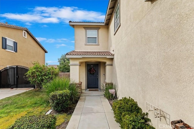 property entrance with a gate, a tile roof, and stucco siding