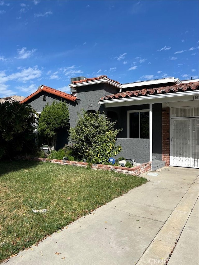 view of front facade featuring a tiled roof, a front yard, and stucco siding