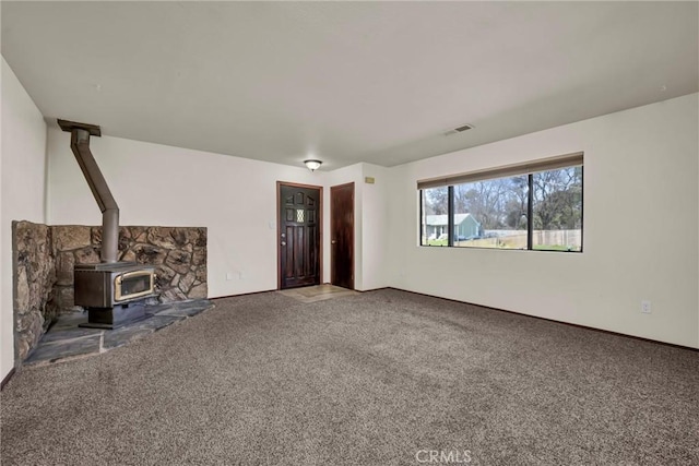 unfurnished living room featuring a wood stove, visible vents, and carpet flooring