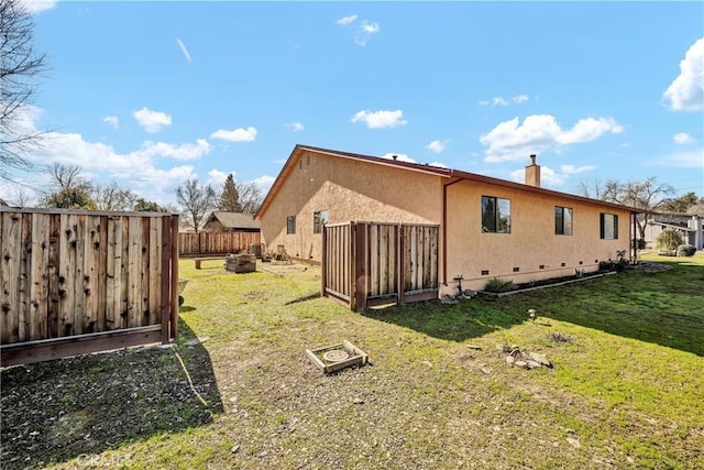 back of property with a fenced backyard, a chimney, crawl space, a yard, and stucco siding