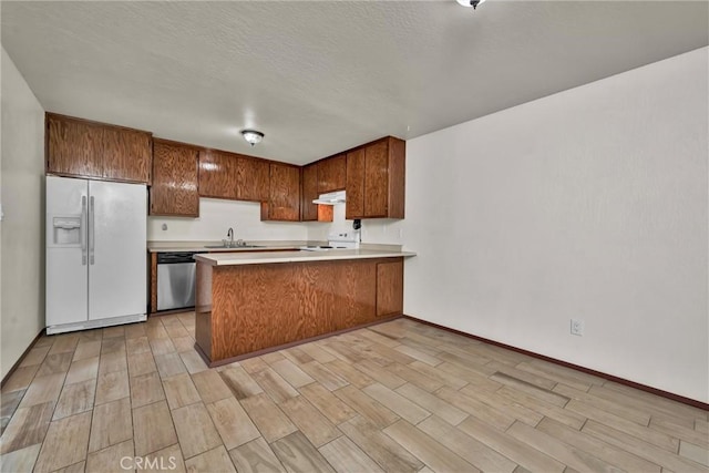 kitchen with under cabinet range hood, a peninsula, white refrigerator with ice dispenser, brown cabinets, and dishwasher