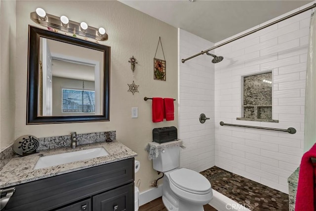 bathroom featuring baseboards, tiled shower, vanity, and toilet