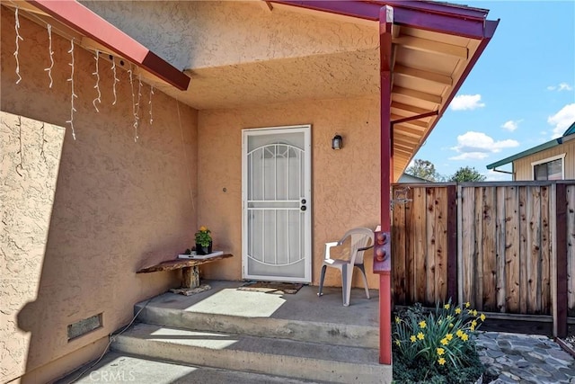 view of exterior entry featuring crawl space, fence, and stucco siding