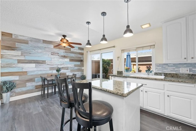 kitchen with an accent wall, white cabinets, a sink, and dark wood-type flooring