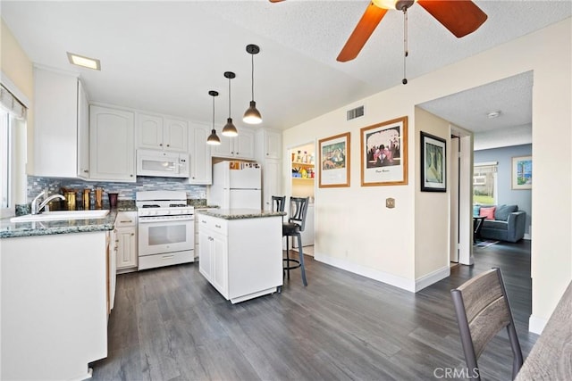 kitchen with white appliances, a kitchen island, visible vents, and white cabinets