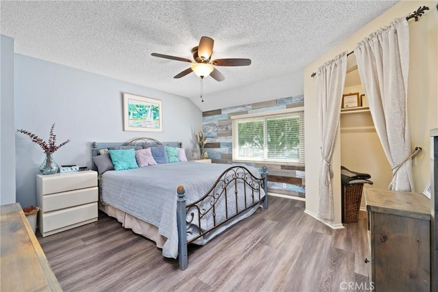 bedroom featuring a textured ceiling, vaulted ceiling, wood finished floors, and a ceiling fan