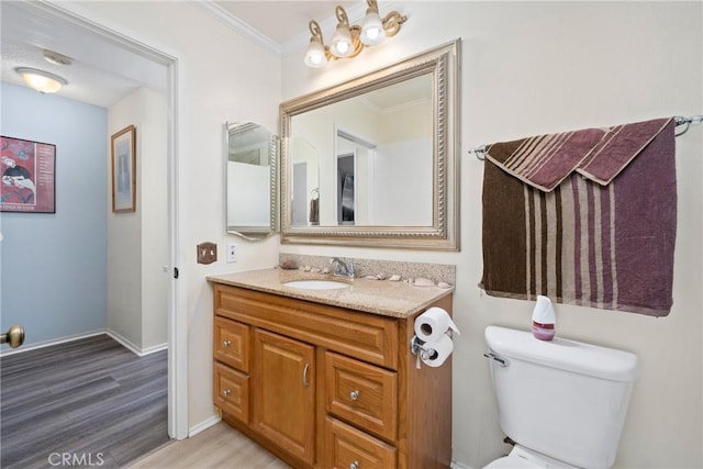 bathroom featuring crown molding, toilet, vanity, wood finished floors, and baseboards