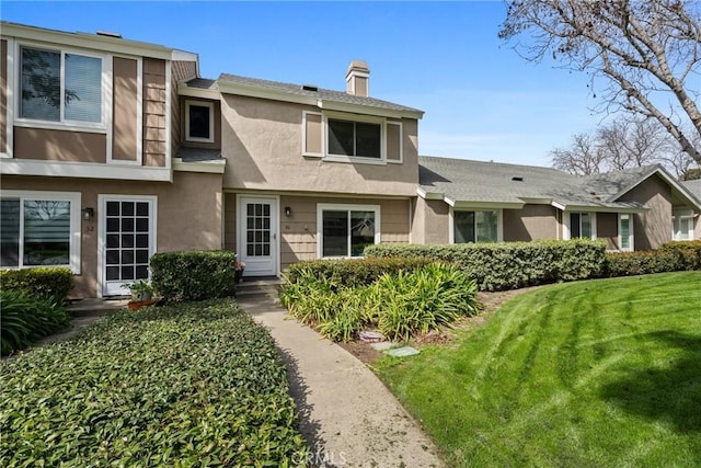 townhome / multi-family property featuring a chimney, a front yard, and stucco siding