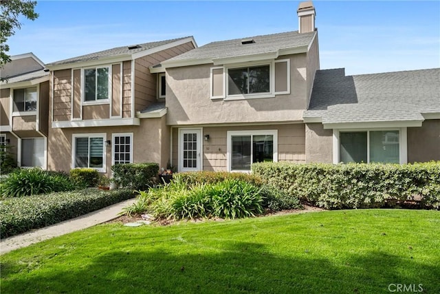 townhome / multi-family property with a shingled roof, a front yard, a chimney, and stucco siding