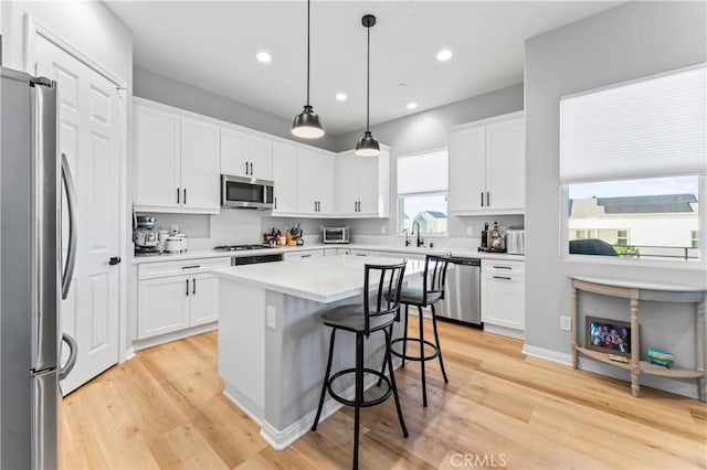 kitchen featuring a center island, light wood finished floors, stainless steel appliances, white cabinets, and a kitchen breakfast bar