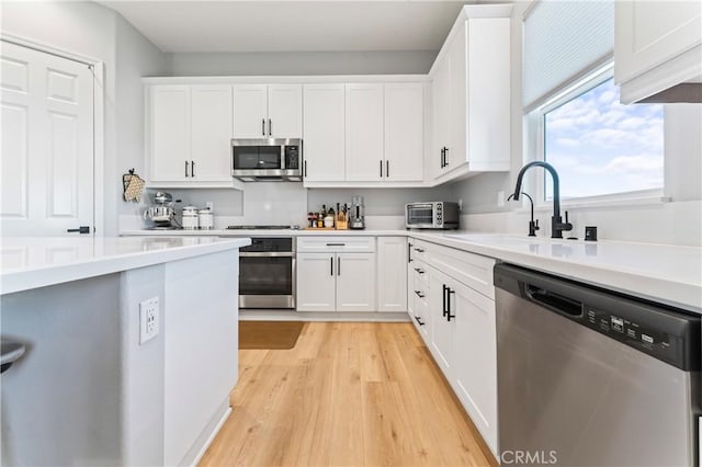 kitchen featuring a sink, light wood-style floors, white cabinets, light countertops, and appliances with stainless steel finishes