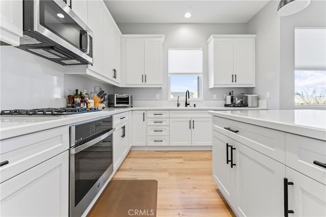 kitchen featuring light countertops, appliances with stainless steel finishes, light wood-style floors, white cabinets, and a sink