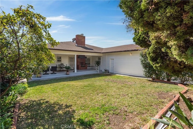 back of house with a chimney, a lawn, and a patio area