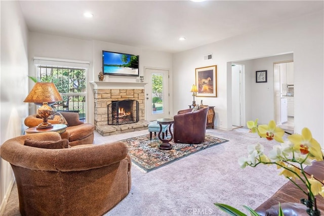 living area with carpet floors, a wealth of natural light, visible vents, and a stone fireplace