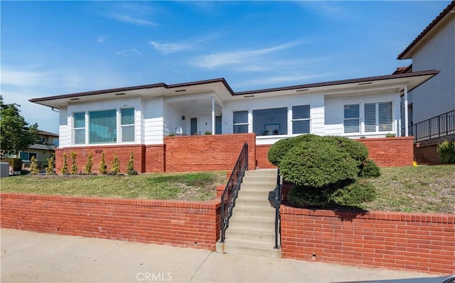 view of front of property with a front yard, brick siding, and stairs