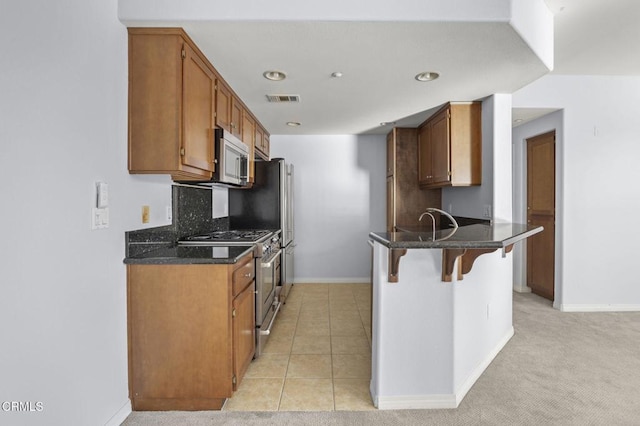 kitchen with light tile patterned floors, stainless steel appliances, a peninsula, visible vents, and a kitchen breakfast bar