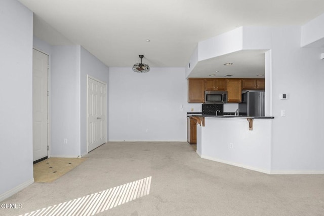 kitchen with a breakfast bar, brown cabinets, dark countertops, stainless steel microwave, and freestanding refrigerator