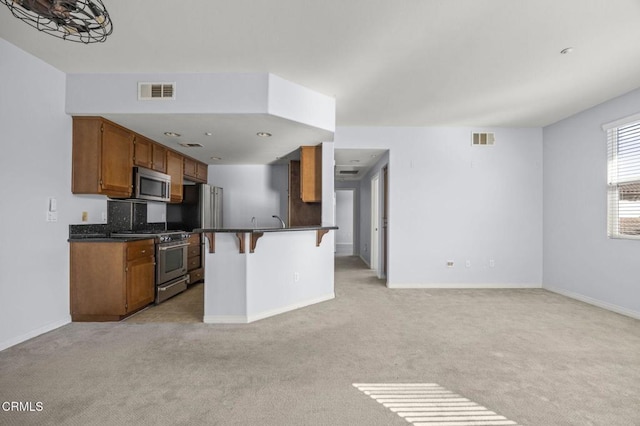 kitchen with light carpet, stainless steel appliances, dark countertops, and visible vents