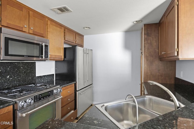 kitchen featuring visible vents, brown cabinetry, dark stone counters, appliances with stainless steel finishes, and a sink