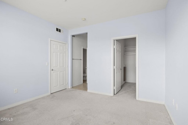 unfurnished bedroom featuring carpet, visible vents, a walk in closet, and baseboards