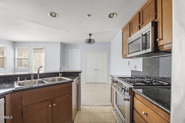 kitchen with appliances with stainless steel finishes, brown cabinets, a sink, backsplash, and light tile patterned flooring