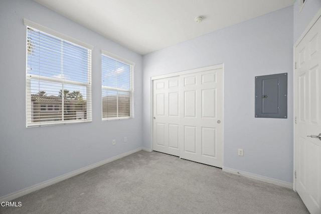 unfurnished bedroom featuring multiple windows, carpet, electric panel, and baseboards