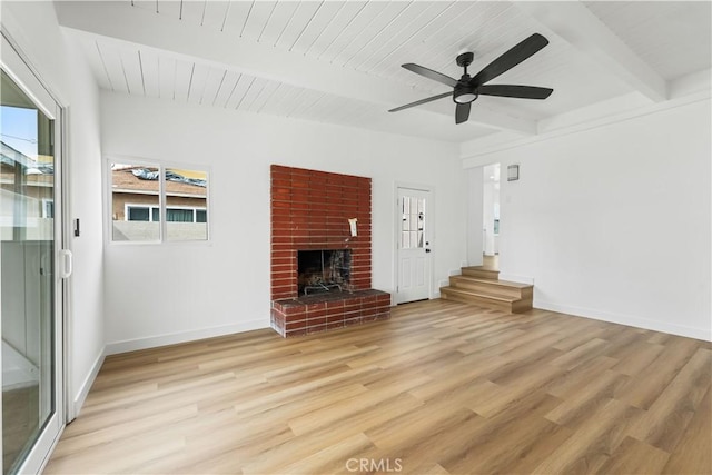 unfurnished living room with baseboards, beamed ceiling, a brick fireplace, and light wood-style floors