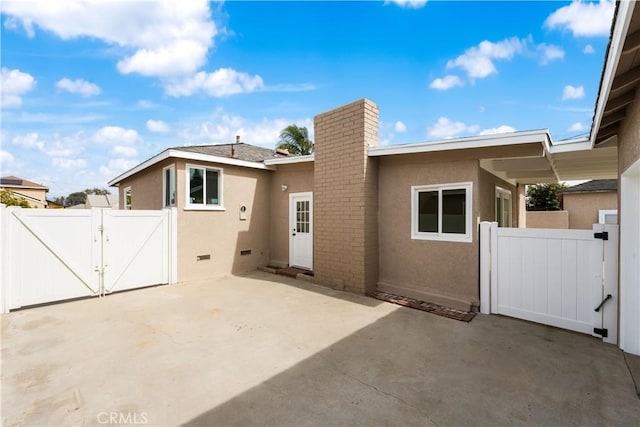 rear view of property with fence, a gate, stucco siding, a chimney, and a patio area