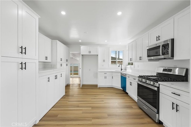 kitchen with appliances with stainless steel finishes, light countertops, a sink, and light wood-style flooring