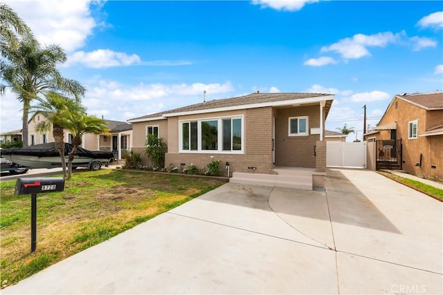 view of front of house featuring driveway, brick siding, a gate, and a front yard