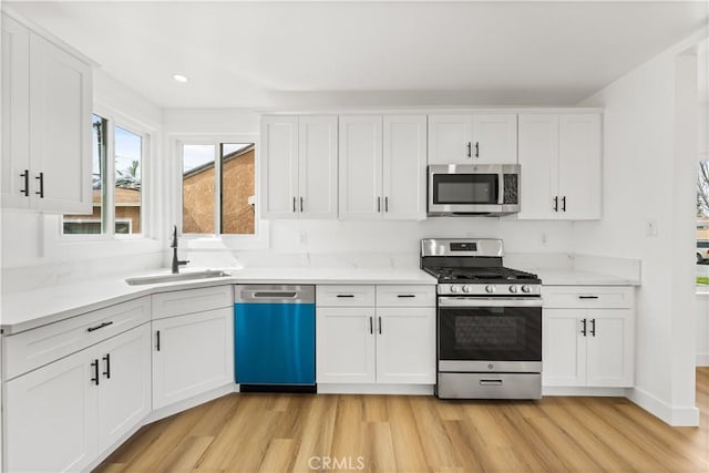 kitchen featuring light wood finished floors, baseboards, stainless steel appliances, white cabinetry, and a sink