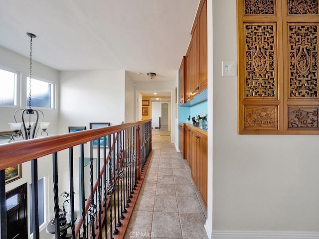 hallway with light tile patterned floors, a notable chandelier, and an upstairs landing